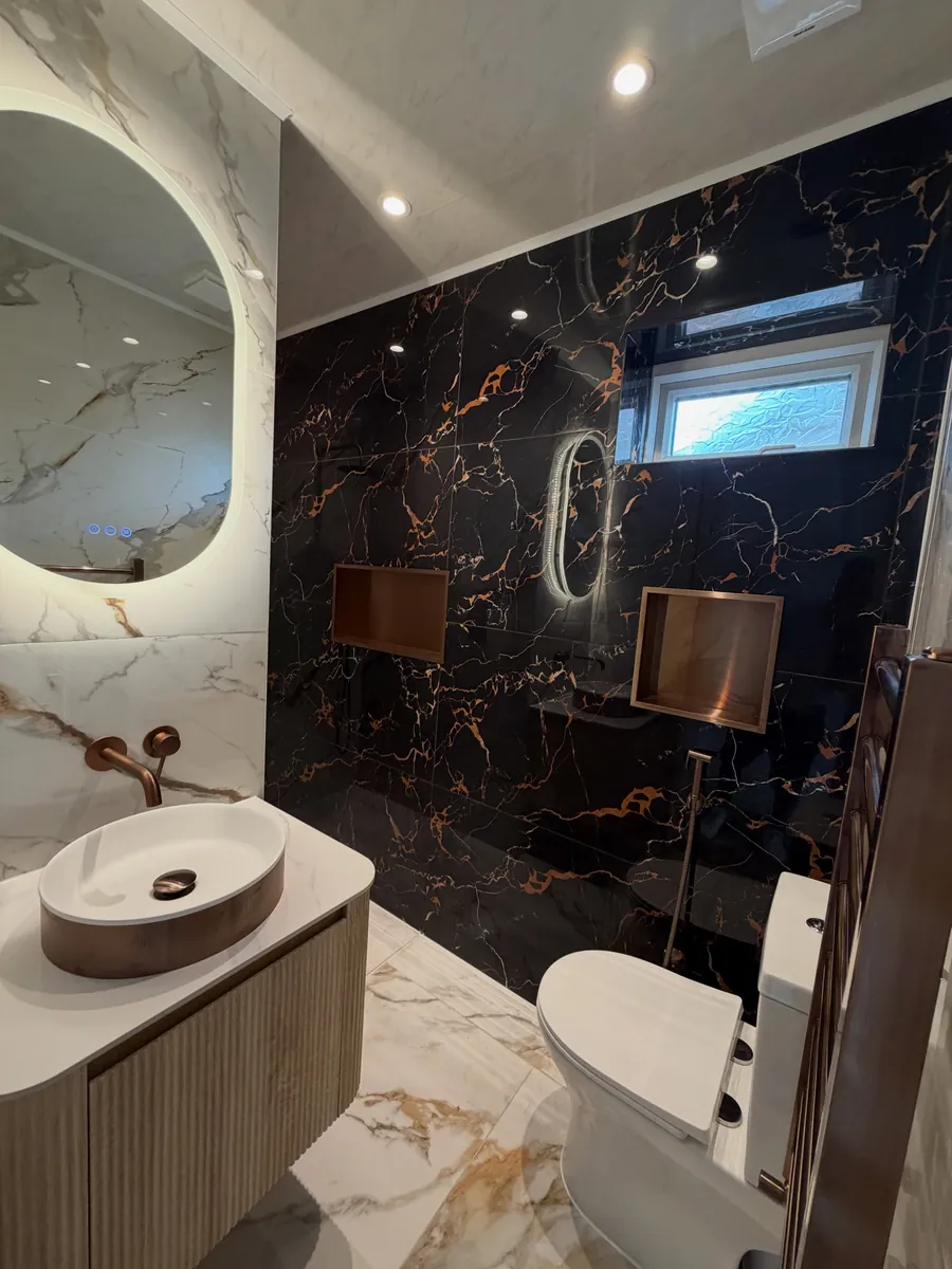 Bathroom with black marble feature wall, oak vanity, copper basin and backlit mirror
