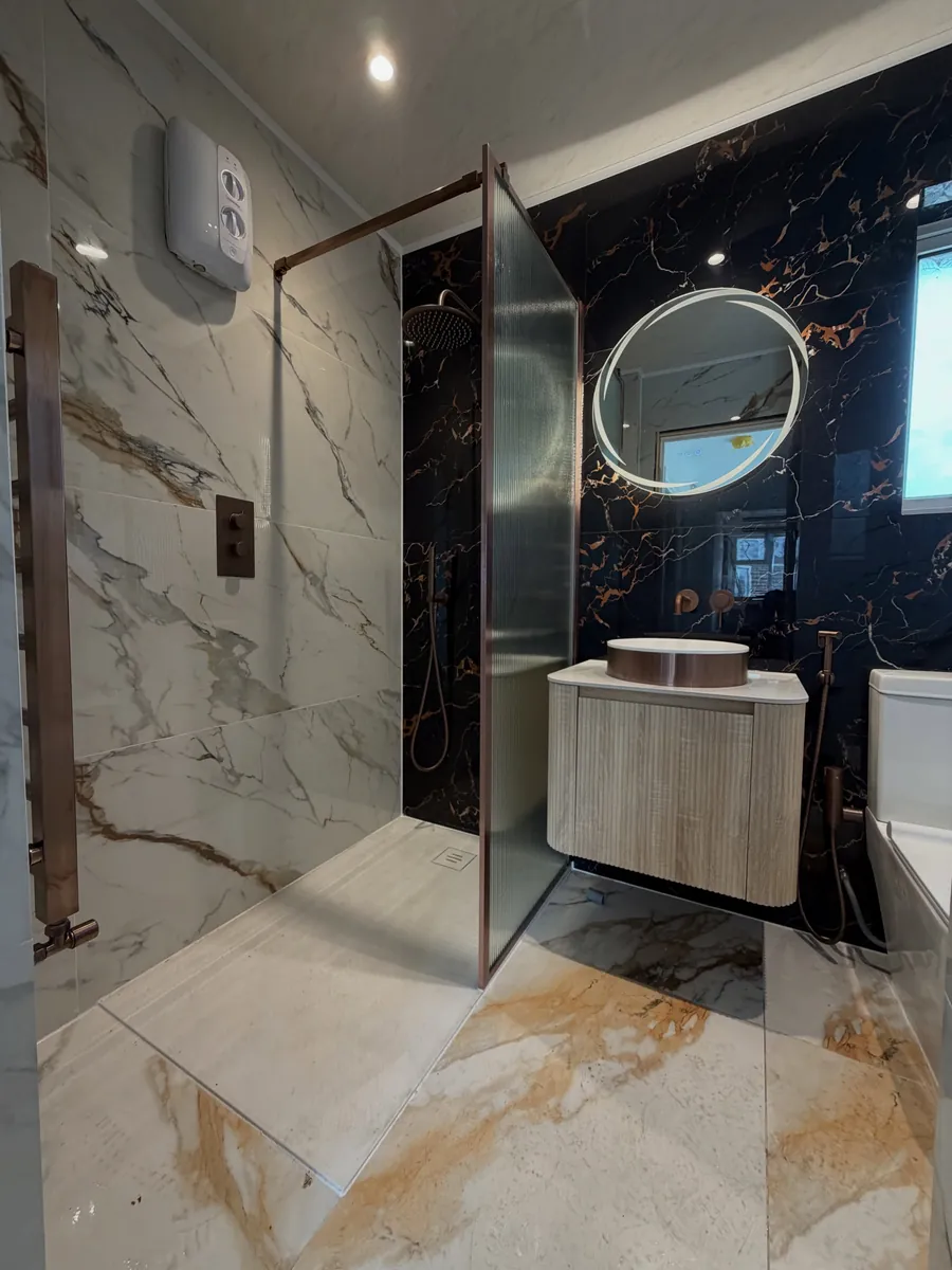 Finished shower room with marble-effect walls, glass screen and backlit round mirror